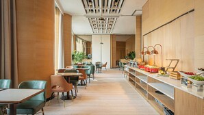 A modern restaurant with wooden flooring, green and brown chairs, and a buffet counter with fruits and vegetables.