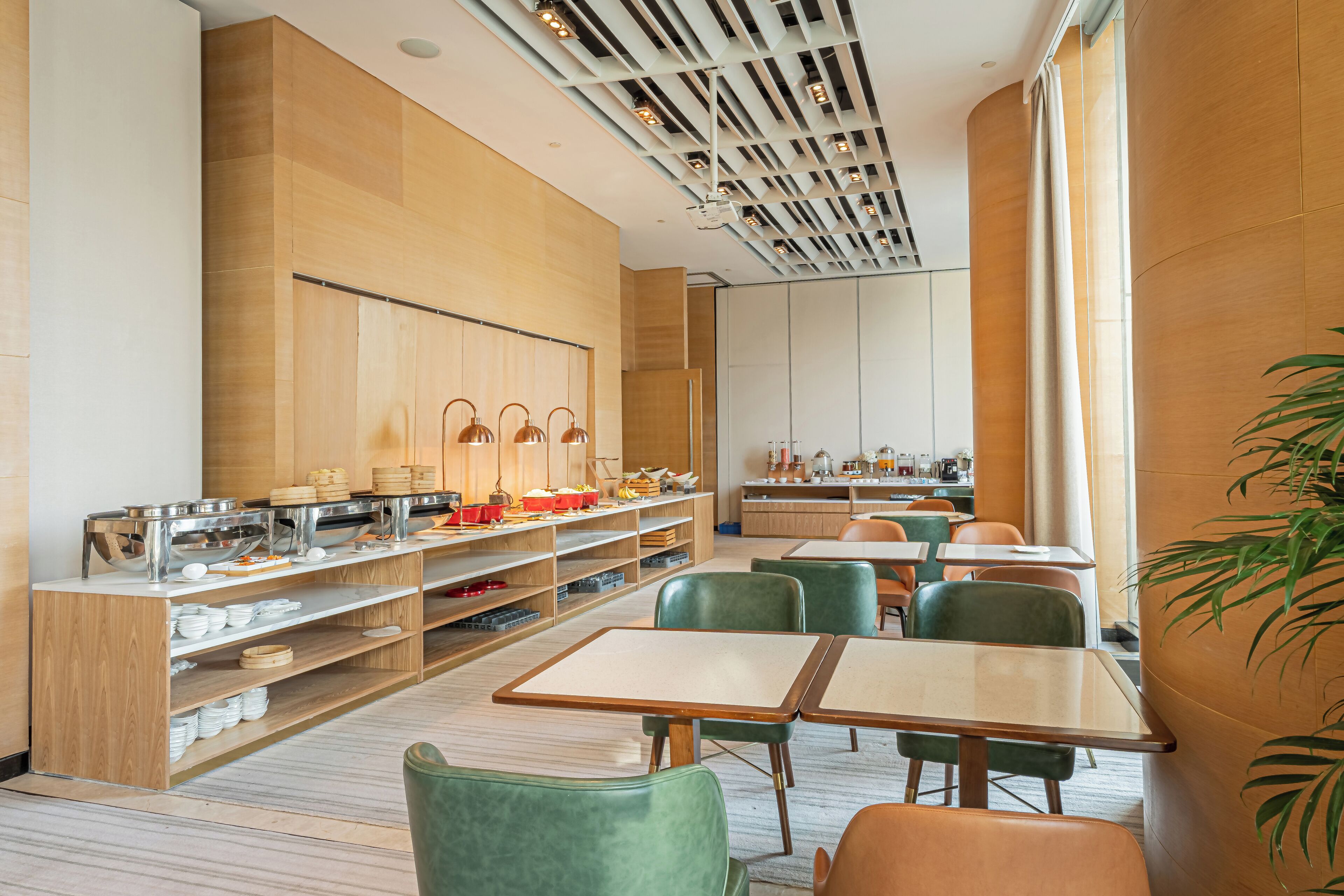 Un espace repas moderne avec un lambris en bois, des comptoirs de buffet en métal et des chaises recouvertes d’un tissu vert.