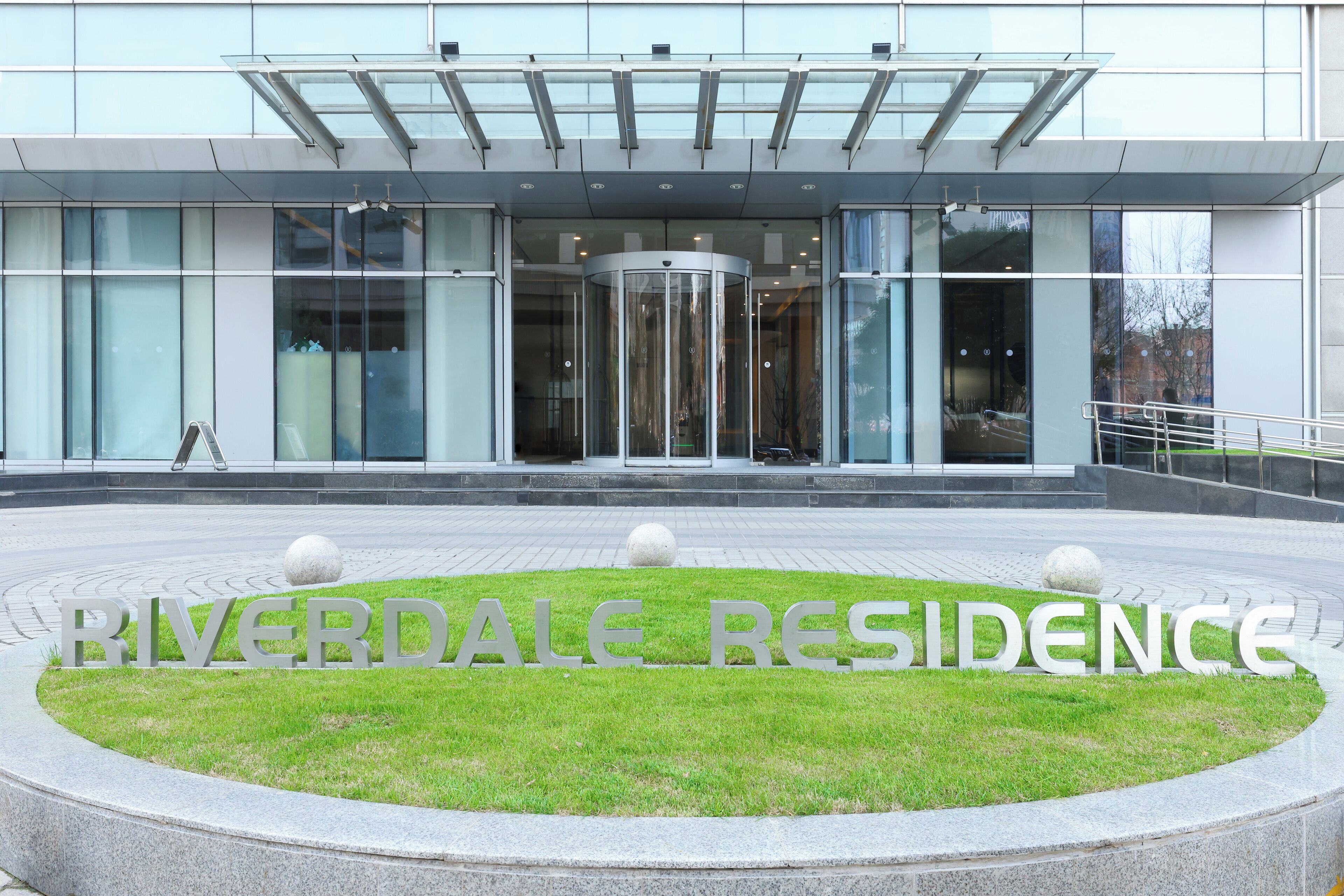 Ein modernes Gebäude mit einer Drehtür, einer Glasfassade und einem Schild mit der Aufschrift 'RIVERDALE RESIDENCE'.