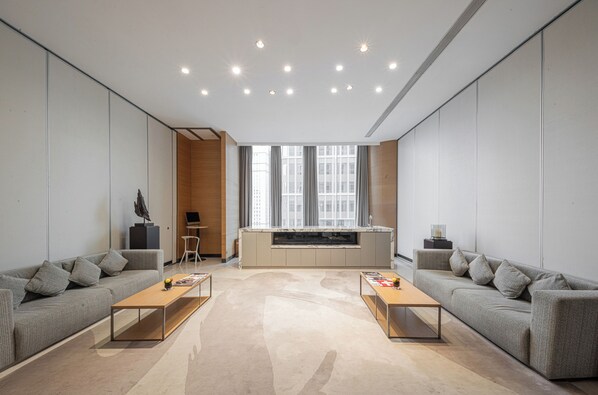 A modern living room with two sofas, a coffee table, a kitchen area, and a large window providing natural light.