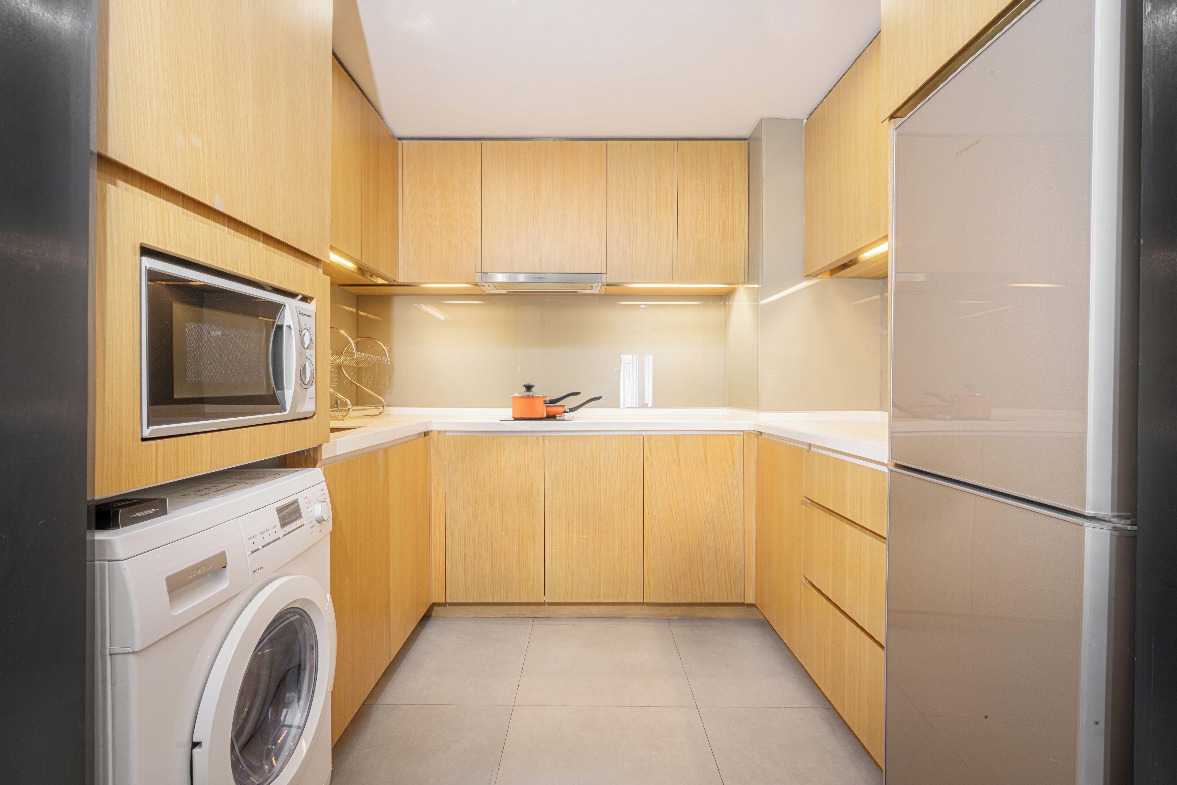 Une cuisine compacte avec des meubles en bois, un four à micro-ondes encastré, un lave-linge et un réfrigérateur.