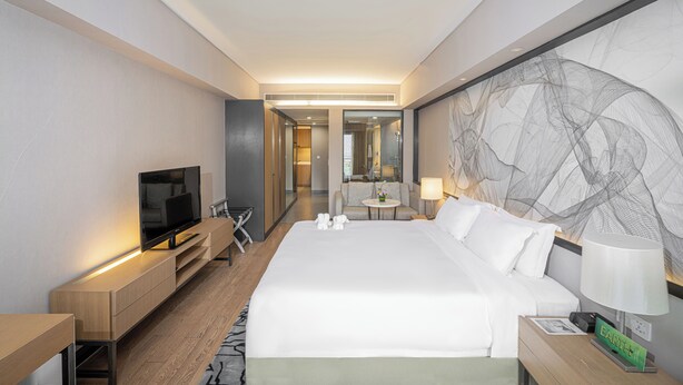 A modern hotel room with a large bed, a flat-screen TV, a desk, and a seating area with a table and chairs.