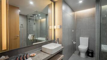 A modern bathroom with a large mirror, a rectangular sink, a toilet, and a glass-enclosed shower area.