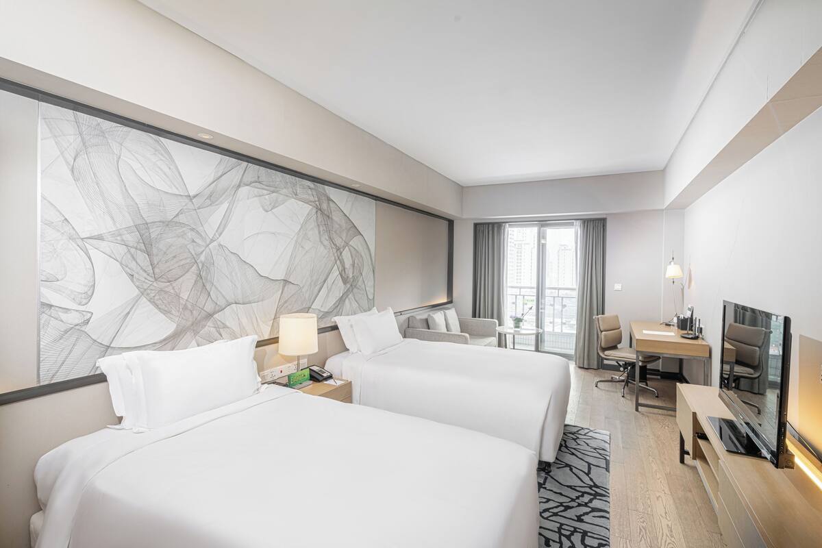 Een hotelkamer met twee bedden, een bureau, een televisie en een groot abstract schilderij aan de muur.