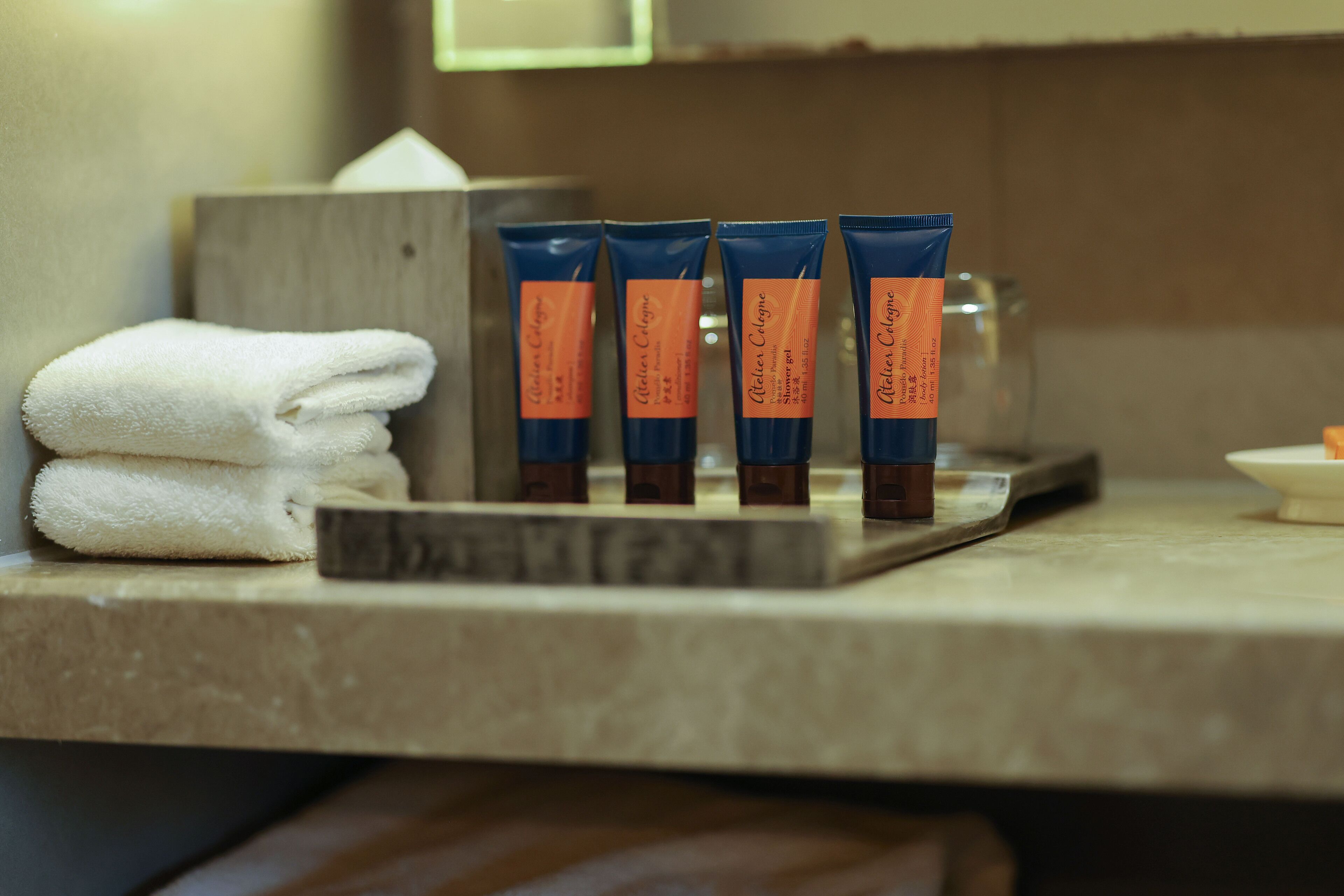A bathroom counter with four tubes of lotion and a stack of towels.