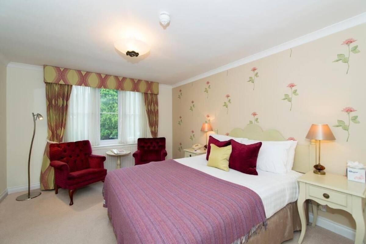 A hotel room with a bed, a chair, a nightstand, a lamp, and a window with curtains.