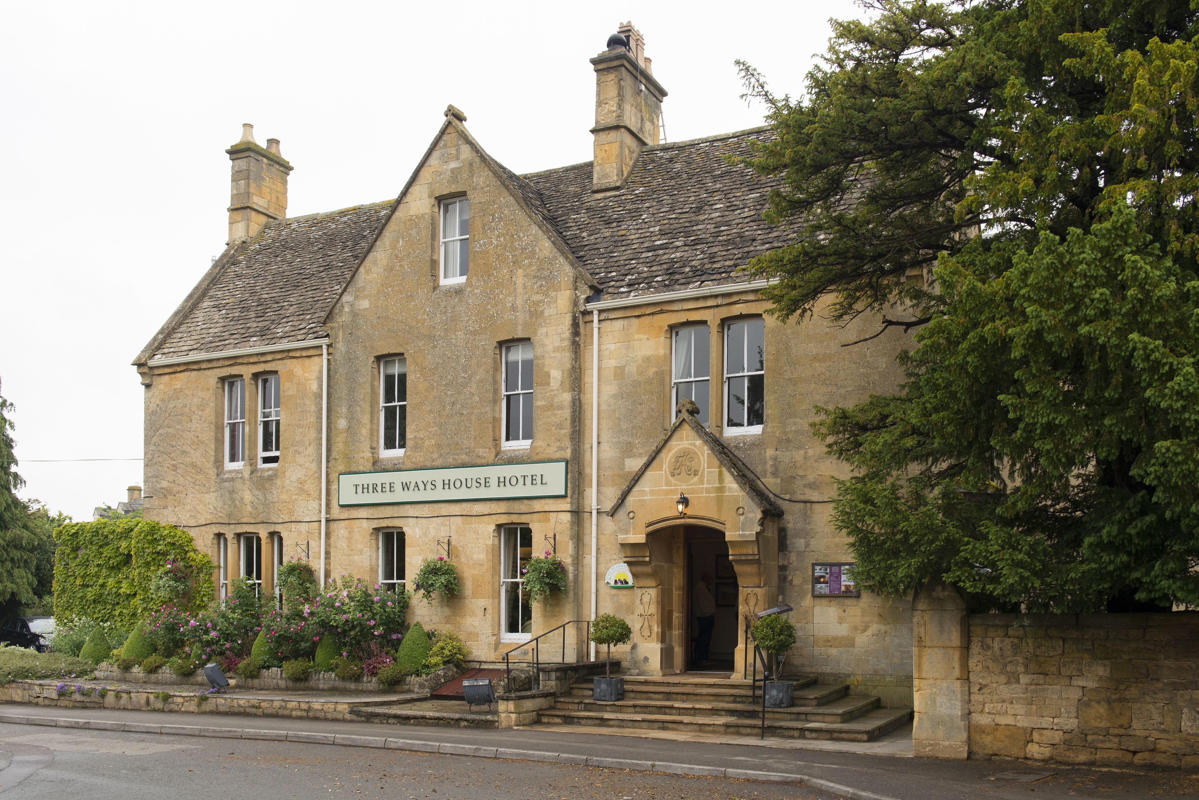 A stone building with a sign reading "Three Ways House Hotel." It features a traditional architectural style with a steeply pitched roof and multiple chimneys.