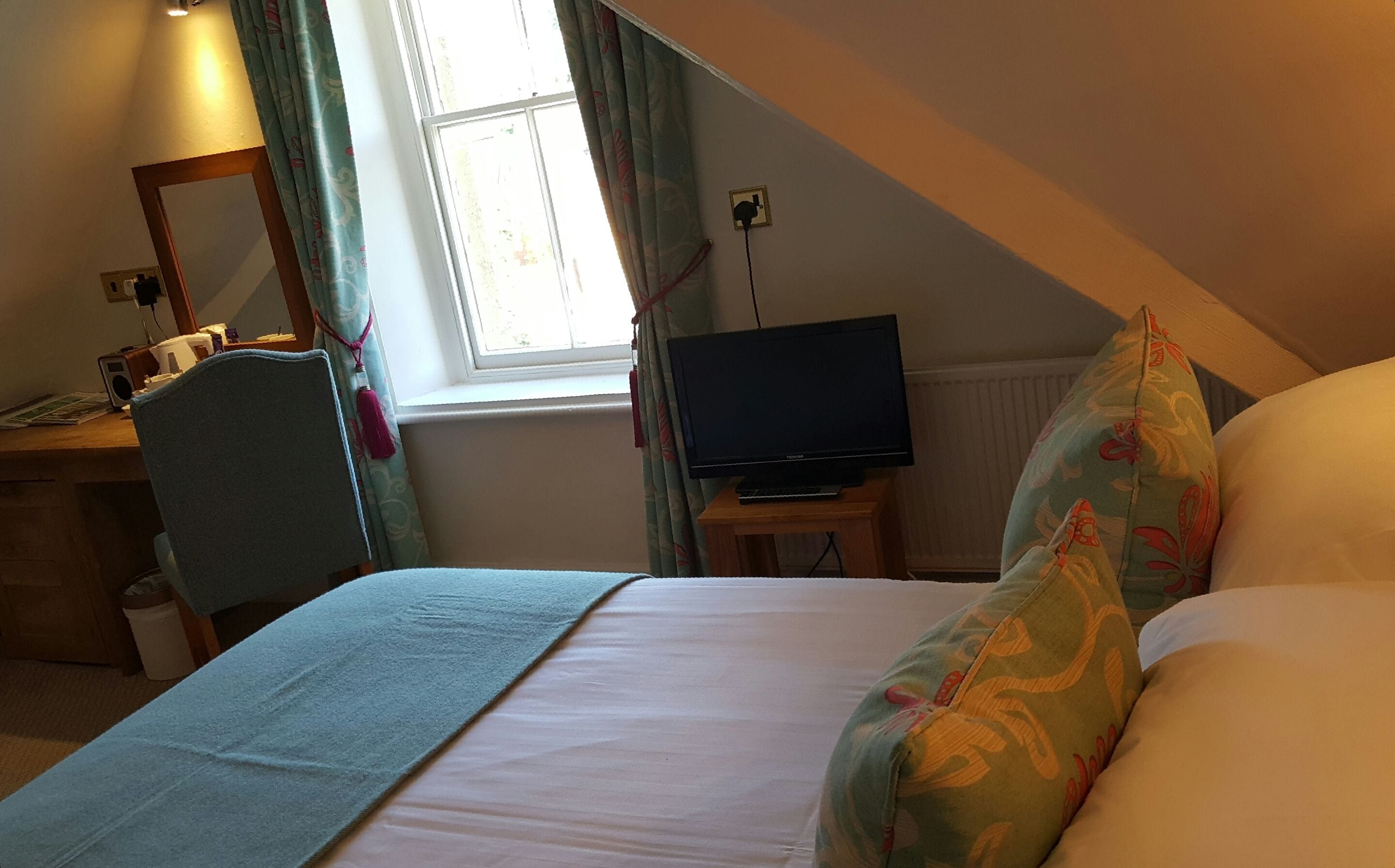 Un dormitorio con una cama, un escritorio con ordenador, una televisión y una ventana con cortinas.