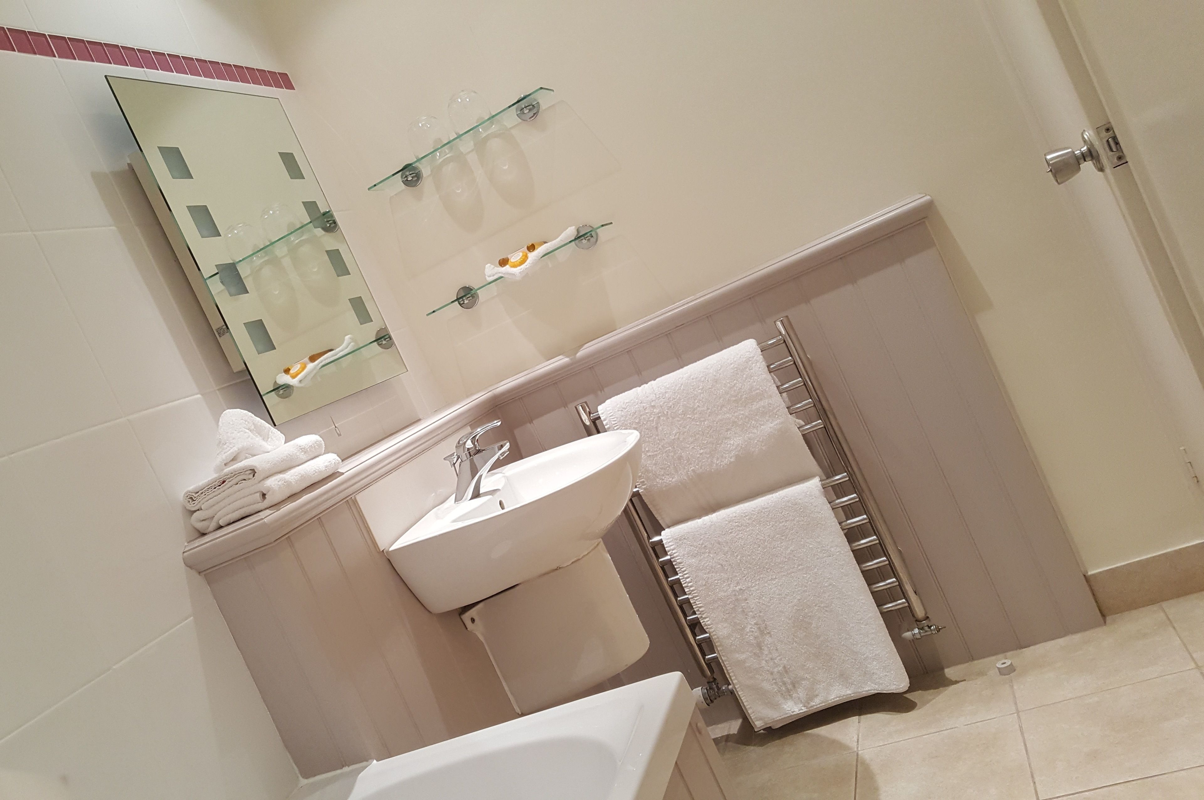Un baño con lavamanos, espejo y toallero.