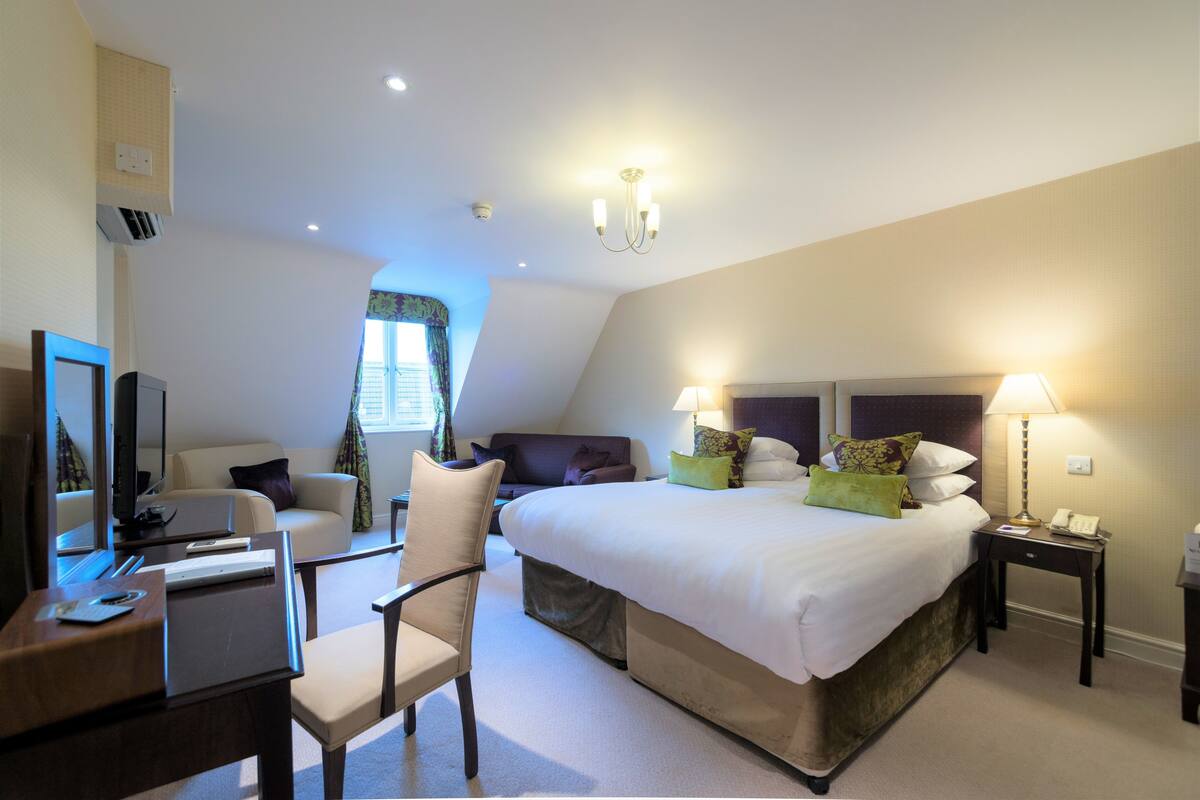 A hotel room with a bed, a desk, a chair, a TV, and a lamp.
