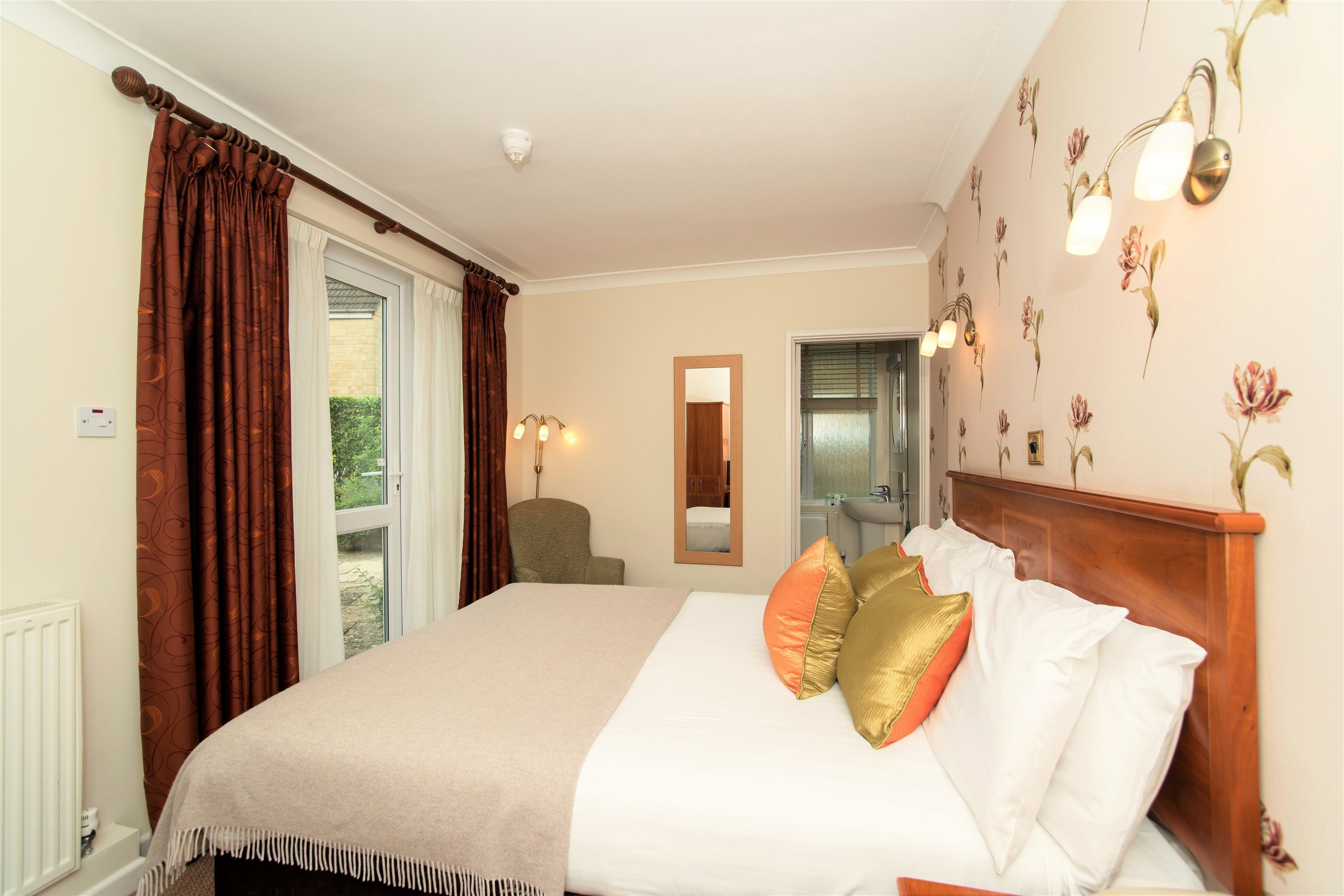 Een hotelkamer met een bed, een stoel, een spiegel en een badkamer, zichtbaar door een open deur.