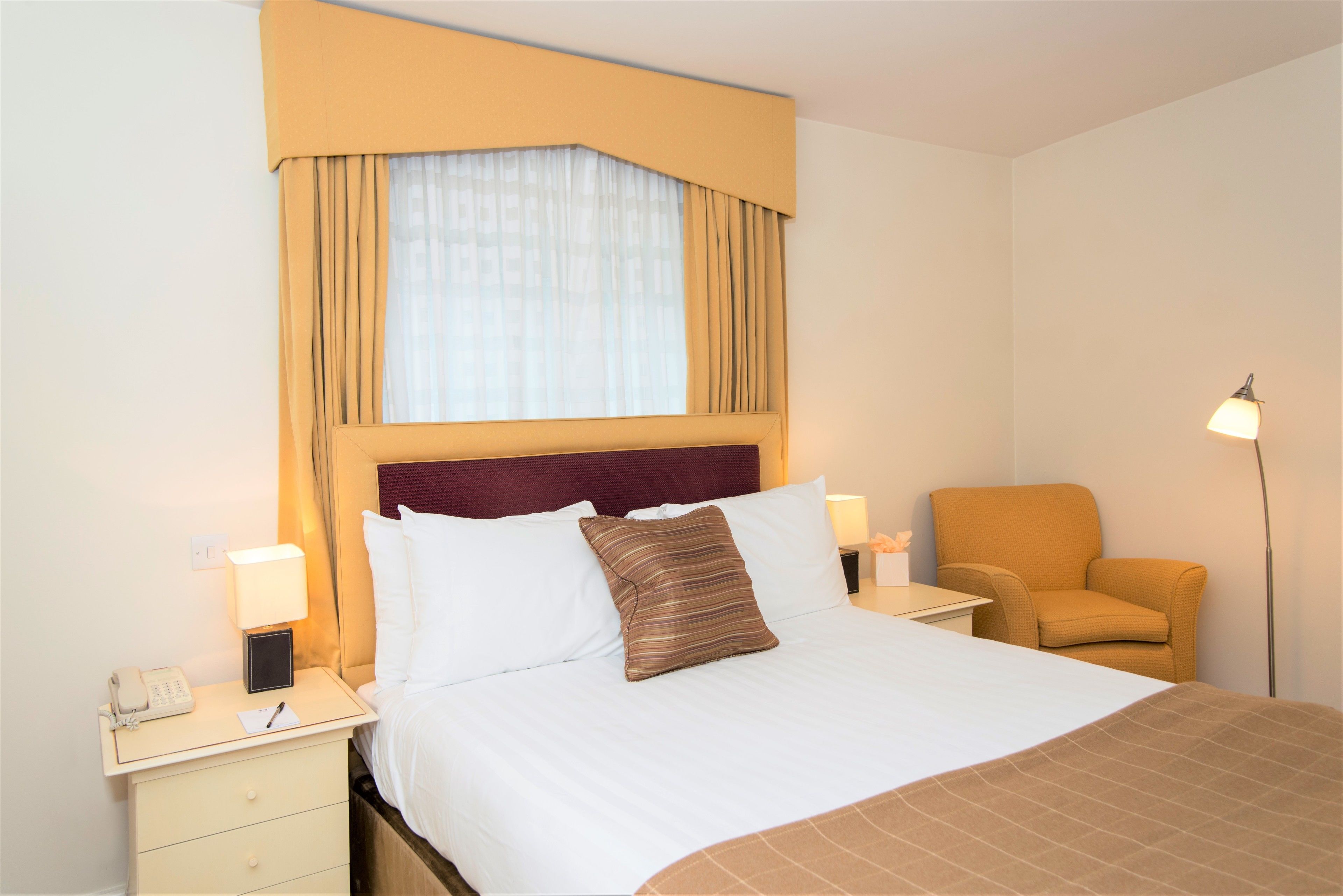 Ein Hotelzimmer mit Bett, Nachttischen, einem Sessel und einer Lampe.