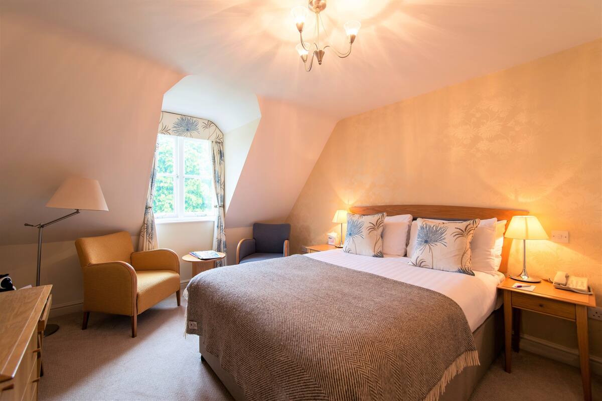A hotel room with a large bed, a chair, a desk, a lamp, and a window with curtains.