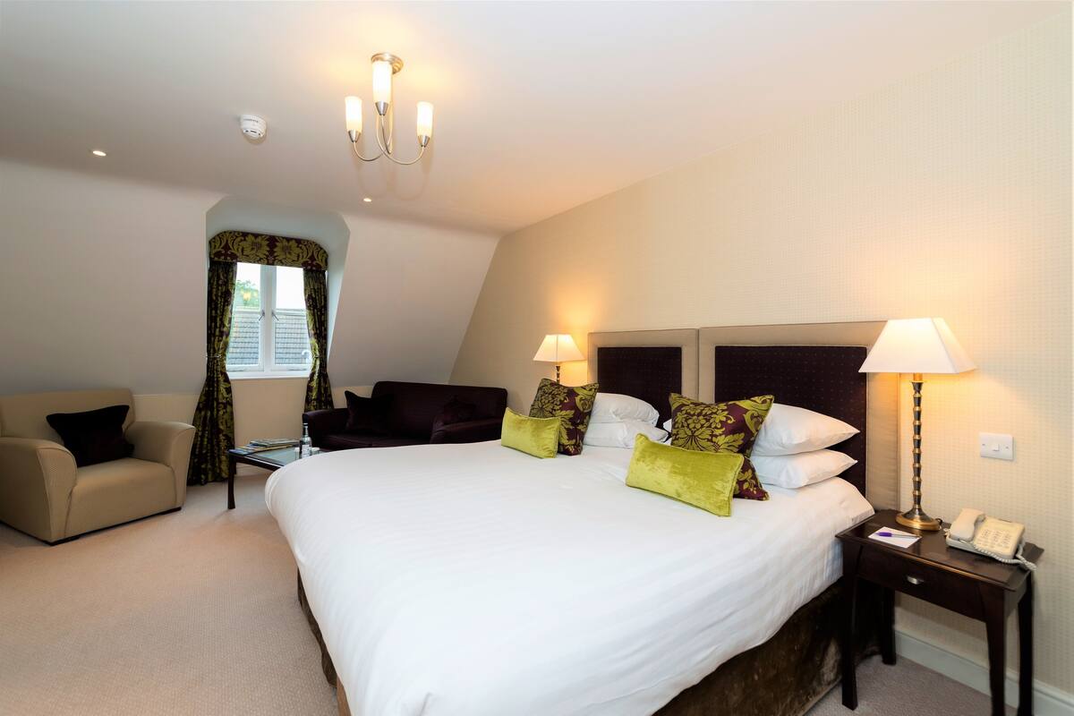 A hotel room with a large bed, two bedside lamps, a desk with a telephone, and a sofa.