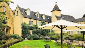 A courtyard with outdoor seating, a garden, and a building with multiple windows and a tower. - Three Ways House Hotel (Chipping Campden)