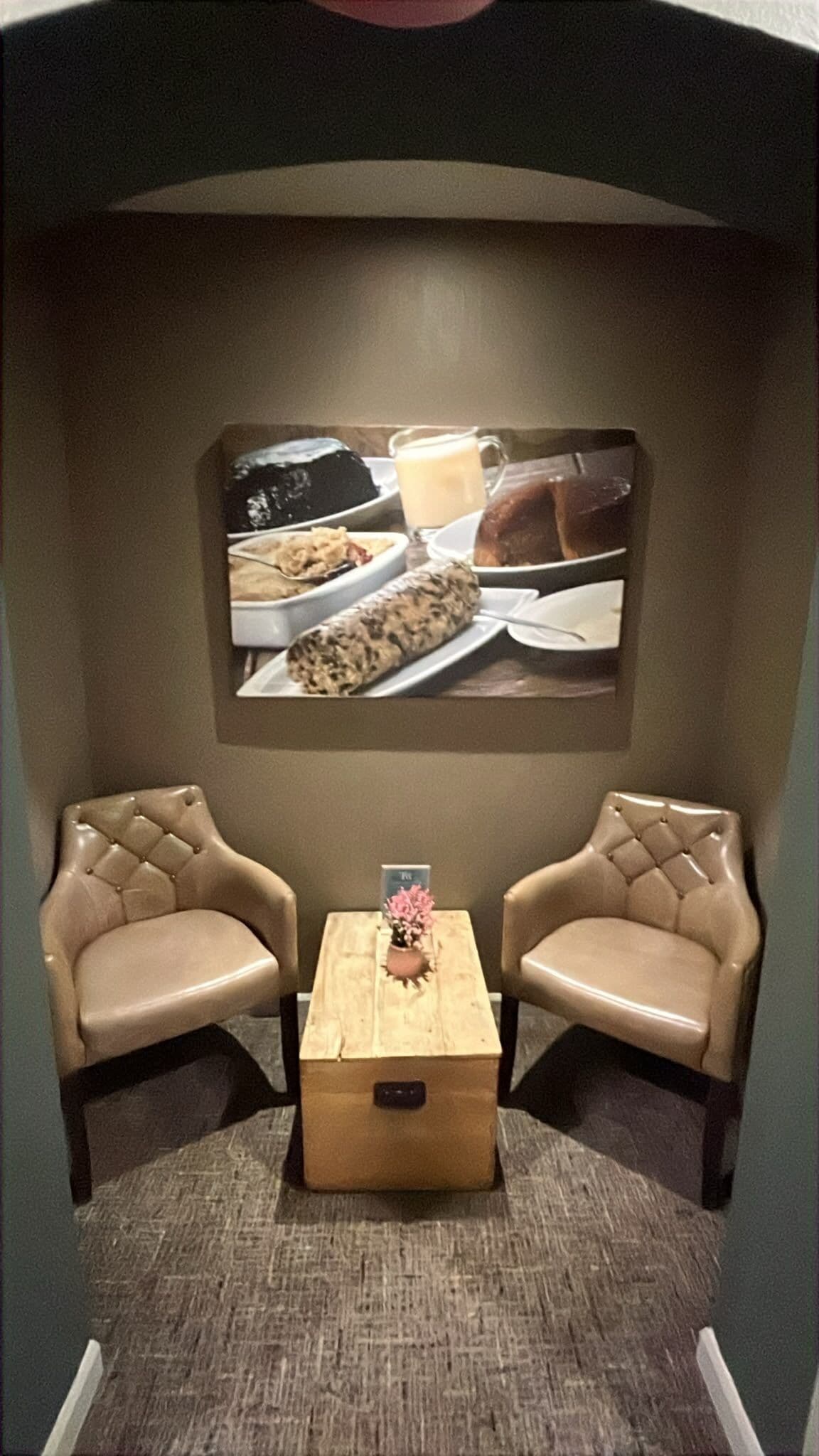 A small room with two leather chairs, a wooden table, and a wall-mounted painting of a meal.