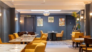 A modern dining area with yellow chairs and tables, a chandelier, and artwork on the walls. - Three Ways House Hotel (Chipping Campden)