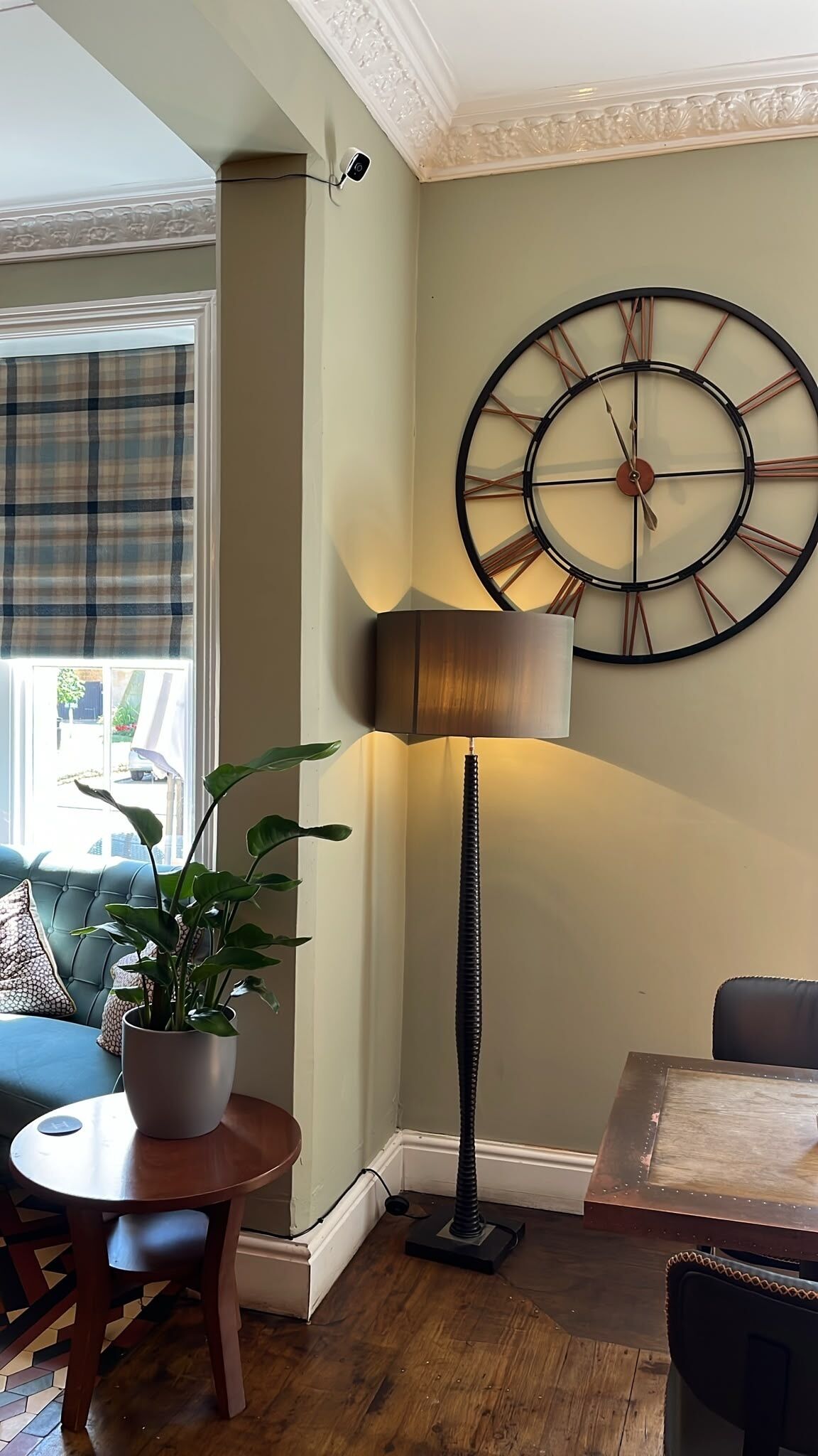 Una habitación con un reloj de pared grande, una lámpara de pie, una planta en maceta y una mesa de comedor.