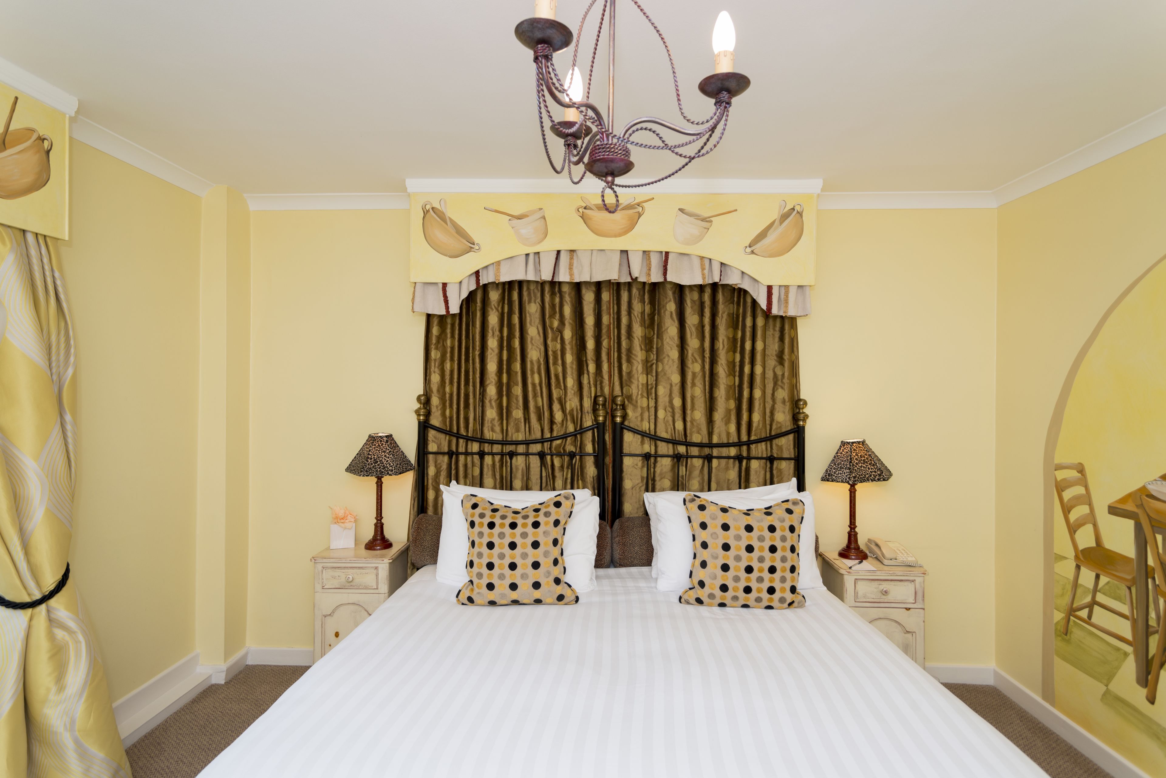 A hotel room with a large bed, two bedside tables with lamps, a chandelier, and a curtain with a pattern.