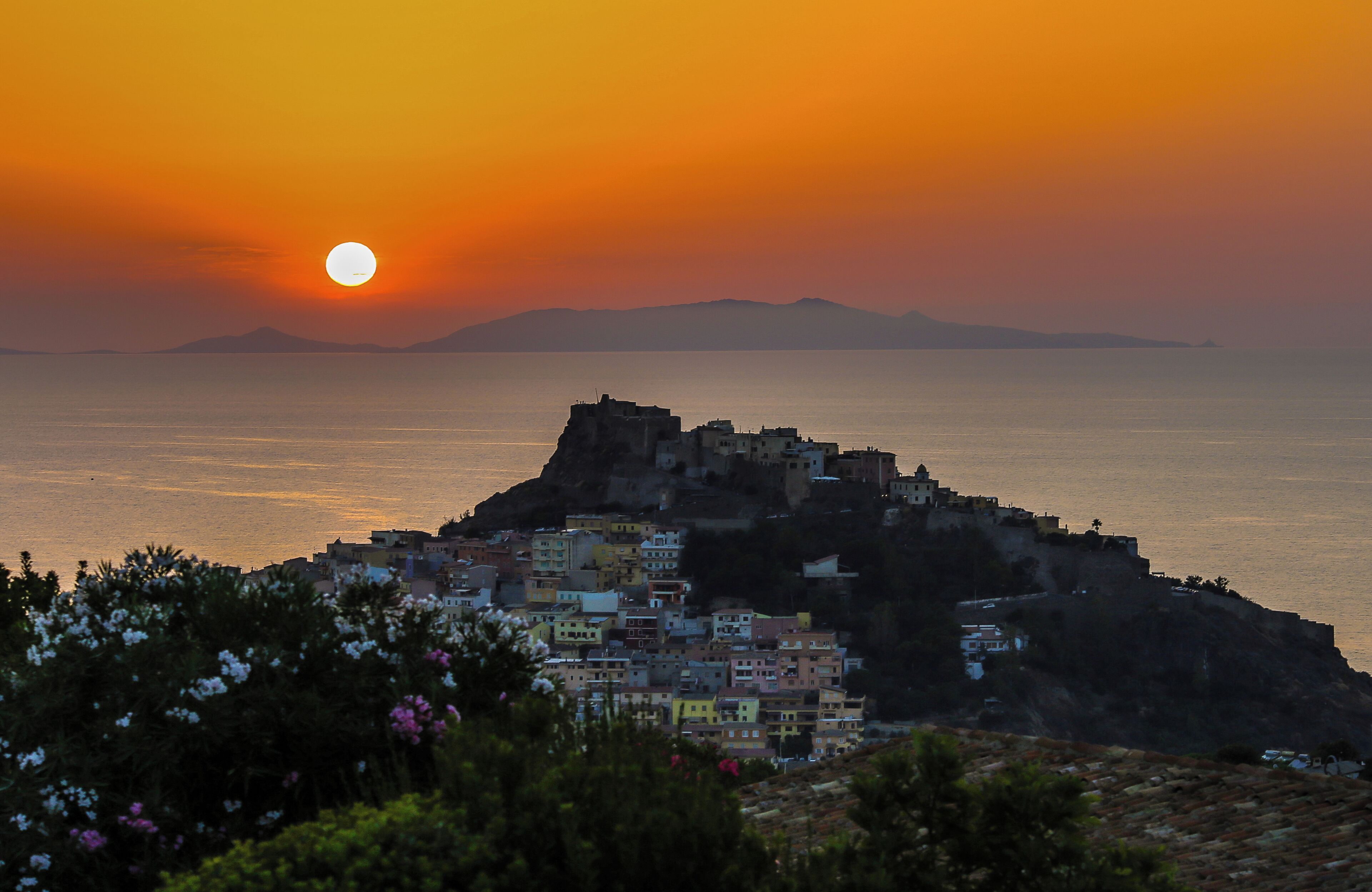 Une ville côtière avec des bâtiments situés sur une colline surplombant la mer, au coucher du soleil.