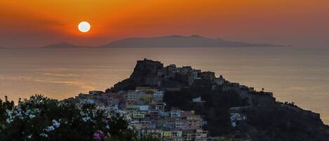 Une ville côtière avec des bâtiments situés sur une colline surplombant la mer, au coucher du soleil.