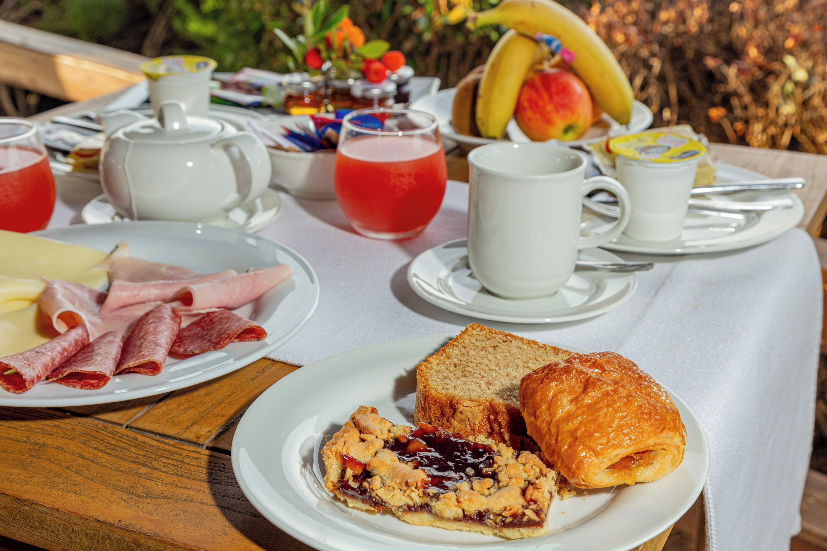 A breakfast setting with plates of food, a teapot, cups, and a table with a view.