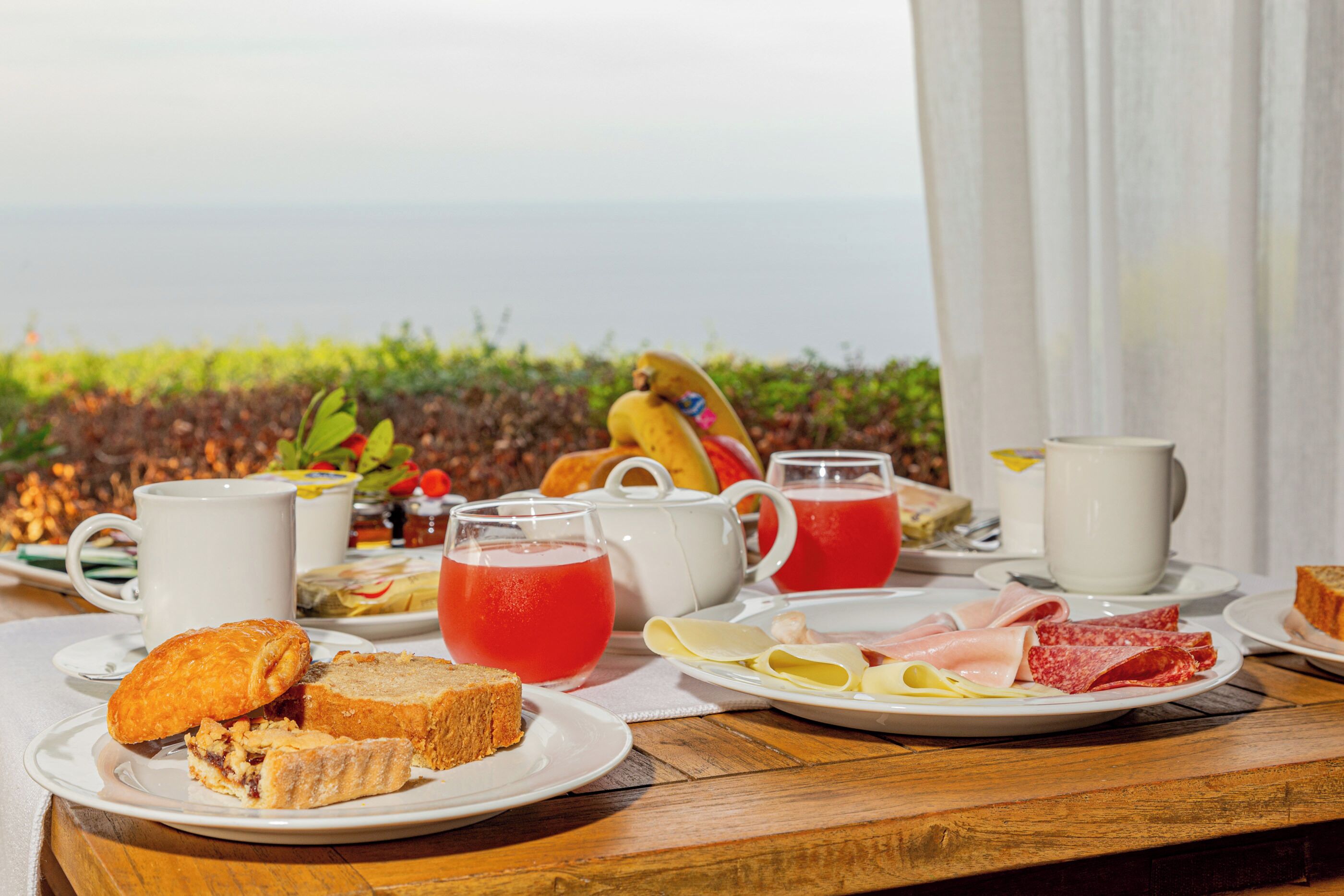 Taula de l'esmorzar amb diferents aliments, una teiera i una tassa, davant d'una vista panoràmica.