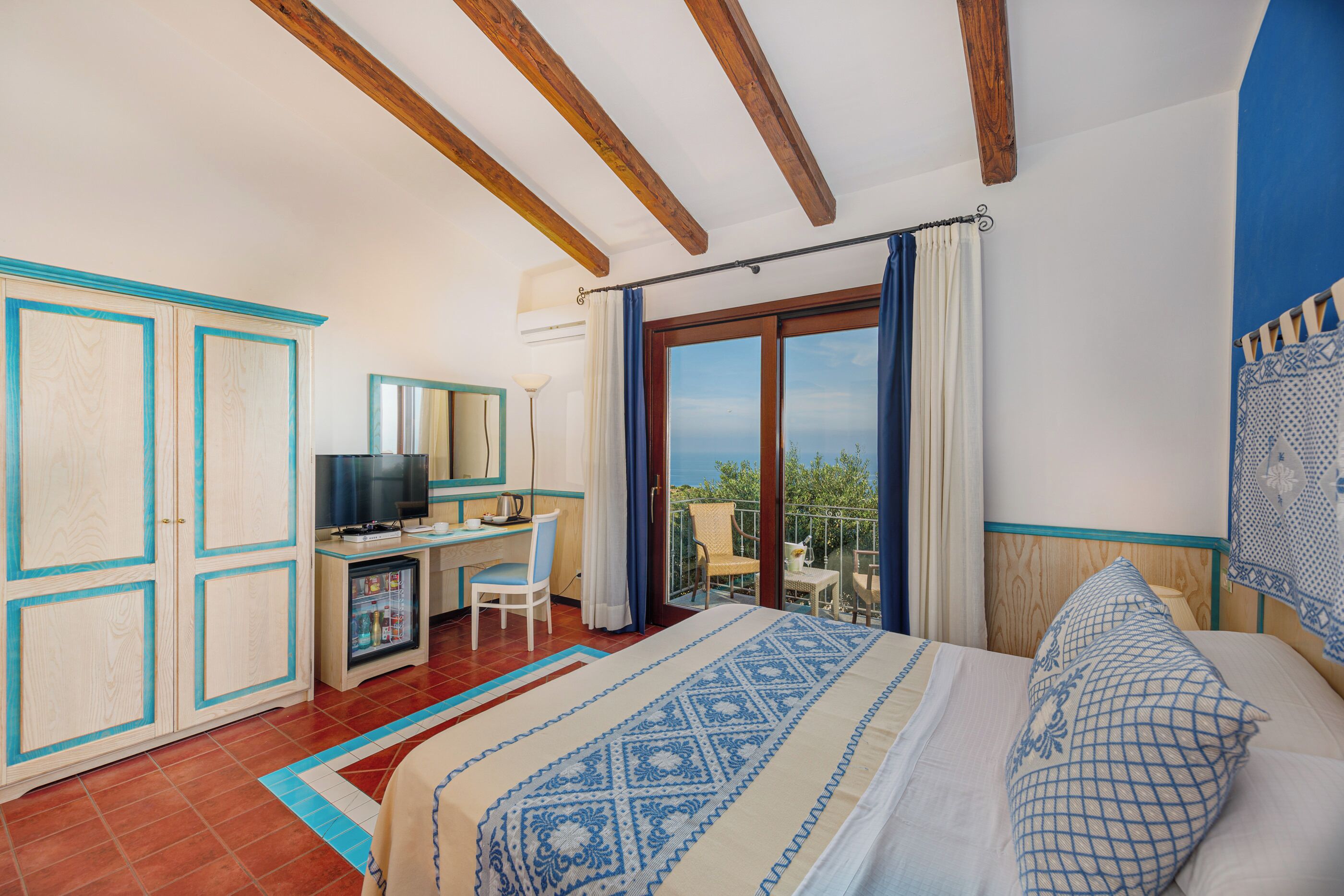 Une chambre avec un lit, un bureau, une télévision et un balcon offrant une vue.