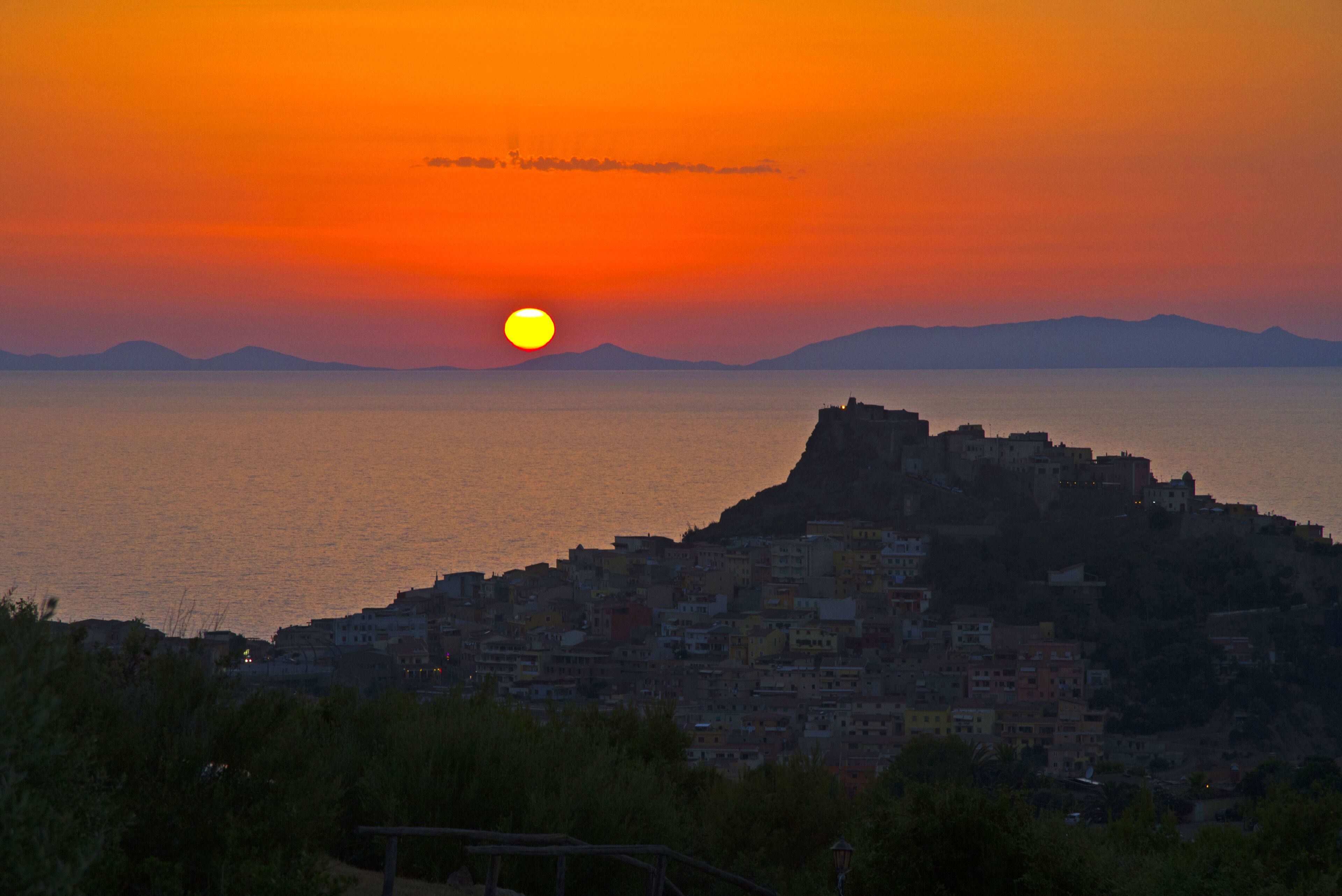 Eine Küstenstadtlandschaft bei Sonnenuntergang mit einem markanten Hügel und Gebäuden.