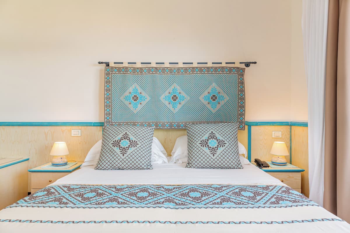 A hotel room with a bed, two bedside tables, a nightstand, and a wall-mounted headboard.