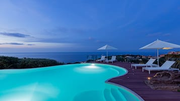 Una piscina al aire libre, sombrillas, sillones reclinables de piscina