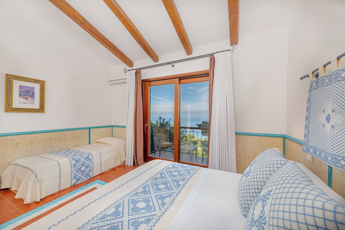 A room with two beds, a balcony with a view, wooden beams on the ceiling, and a framed picture on the wall.