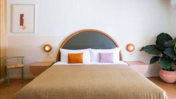 Una cama bien hecha con cabecera de madera, dos mesitas de noche y una planta en maceta.