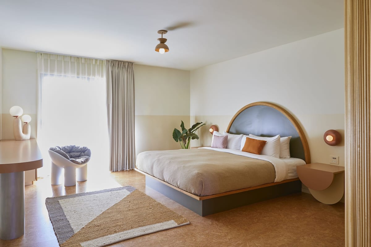 A modern hotel room with a large bed, bedside tables, a desk, and a chair.
