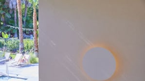 A pool area with lounge chairs and a circular light fixture on a wall.