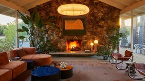 A cozy living room with a stone fireplace, comfortable seating, and a large window overlooking a garden.