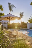 Una piscina al aire libre, sombrillas, sillones reclinables de piscina
