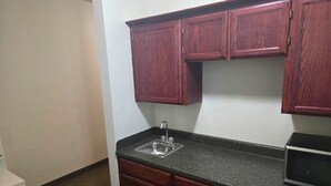 A small kitchen with a granite countertop, a stainless steel sink, and wooden cabinets. - Studio 7 By Capital O Killeen I-14 (Harker Heights)