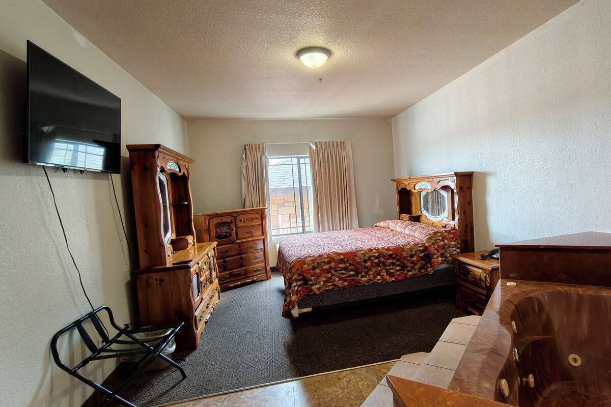 Ein Schlafzimmer mit Bett, einem Holzschrank, einem Schminktisch und einem Fernseher an der Wand.