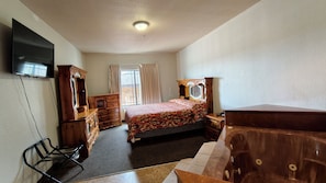 Ein Schlafzimmer mit Bett, einem Holzschrank, einem Schminktisch und einem Fernseher an der Wand.