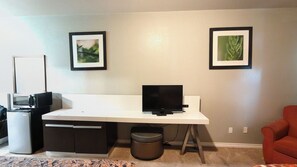 A modern home office with a white desk, a laptop, a microwave, and a trash can.