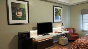 A hotel room with a flat-screen TV, two beds, a small cabinet, a chair, and framed pictures on the wall. - Studio 7 By Capital O Killeen I-14 (Harker Heights)