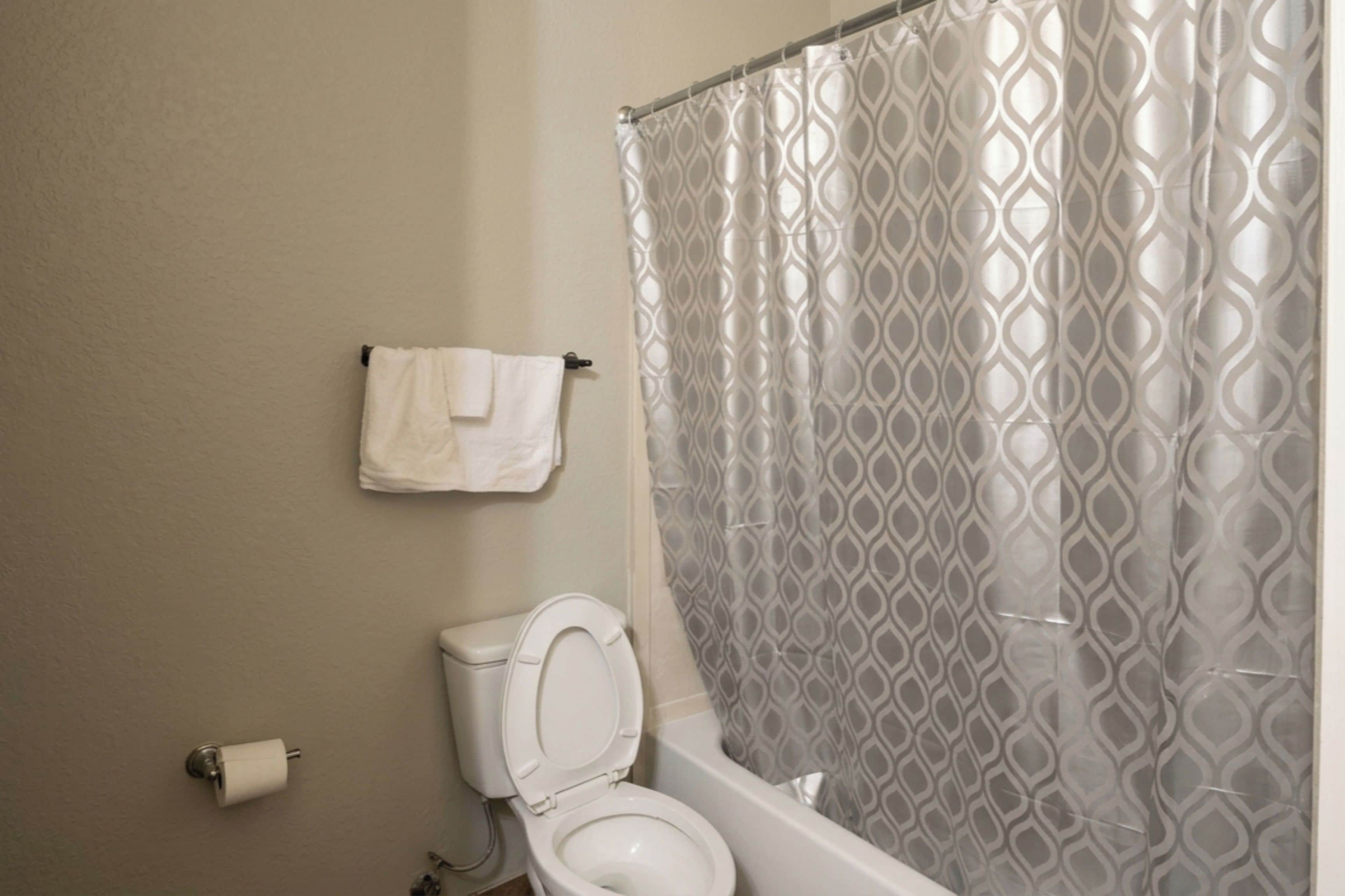Une salle de bain comprenant des toilettes, un porte-serviettes avec une serviette, et un rideau de douche orné d’un motif géométrique.