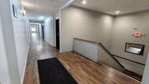 Un pasillo largo y estrecho con piso de madera, una felpudo negro, una barandilla y una señal de salida.
