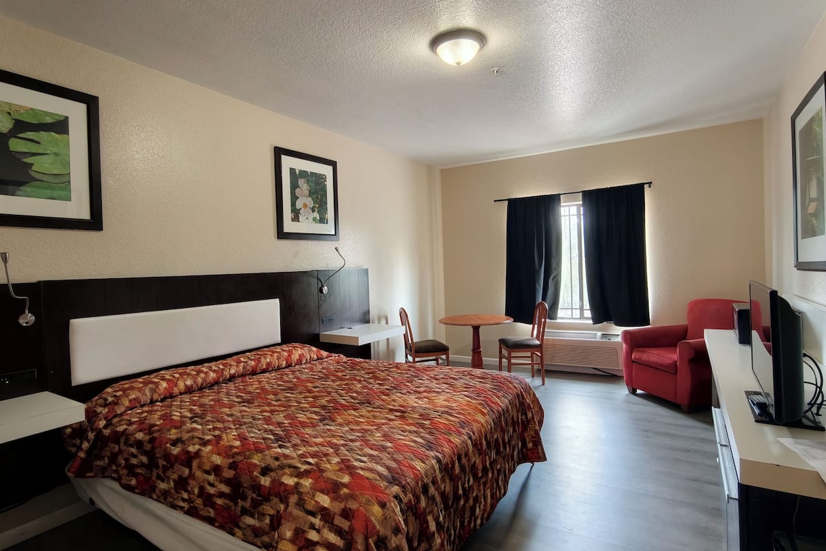 Ein Hotelzimmer mit Bett, Schreibtisch, Stuhl, Fernseher und einem Fenster mit Vorhängen.