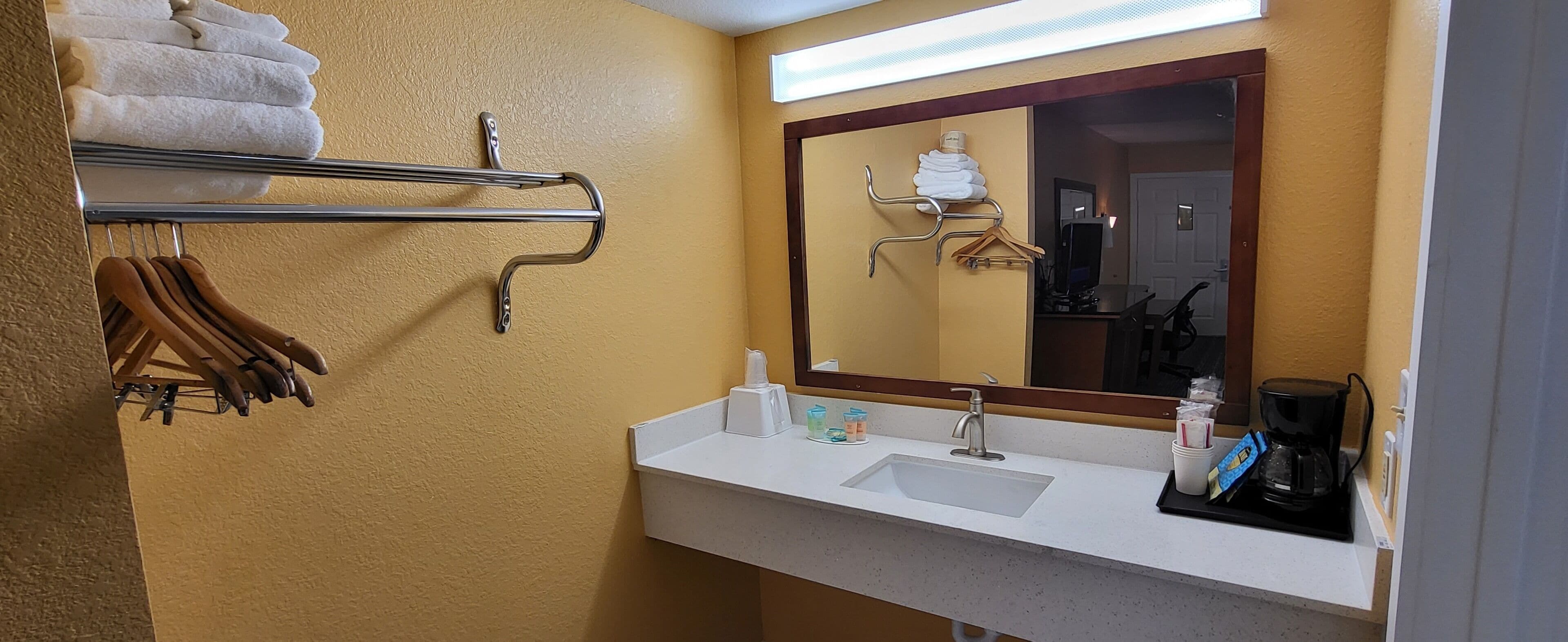 A hotel bathroom with a sink, mirror, towel rack, and toiletries.