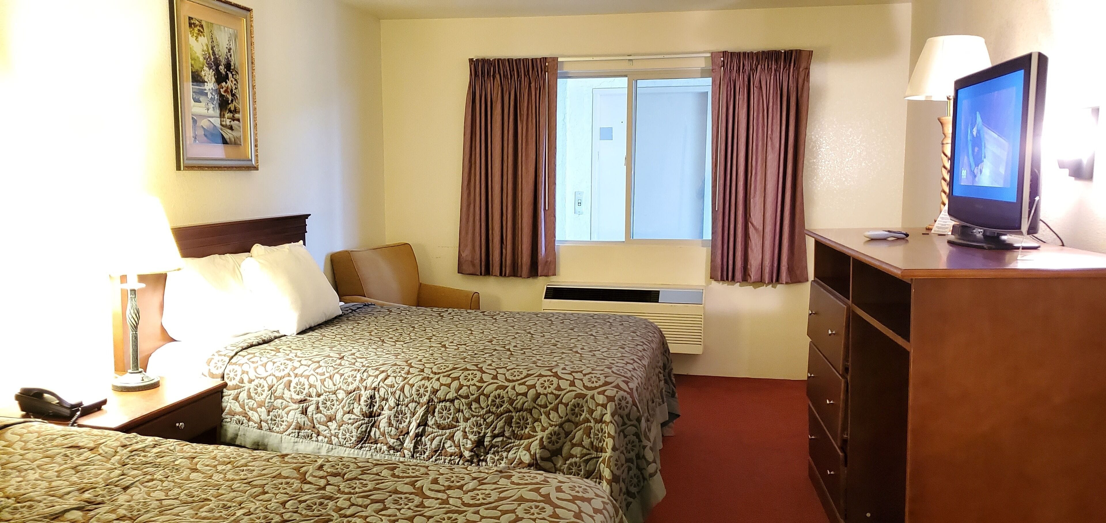 A hotel room with a bed, a desk with a computer, a lamp, and a window with curtains.