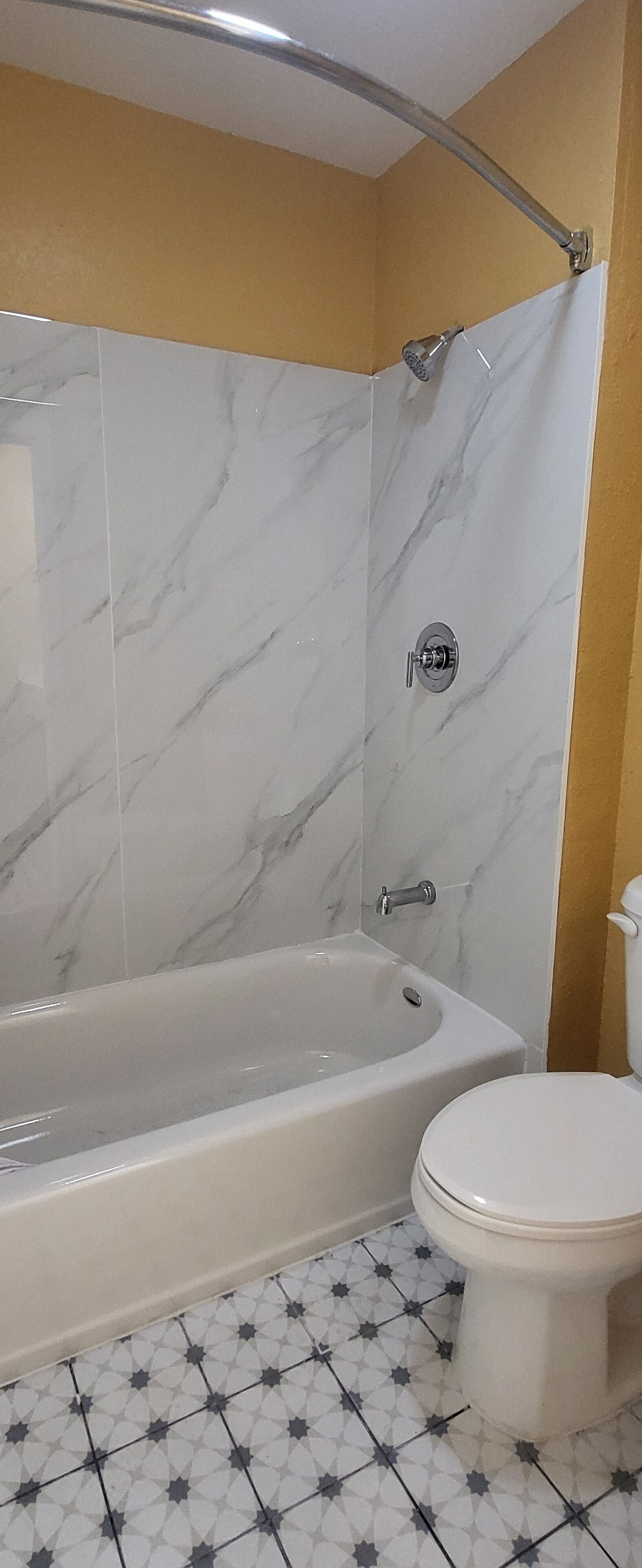A bathroom with a bathtub, toilet, and a shower area with a marble wall.