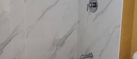 A bathroom with a bathtub, toilet, and a shower area with a marble wall.