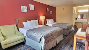Une chambre d’hôtel avec deux lits, un fauteuil vert, un bureau avec une lampe et un miroir.